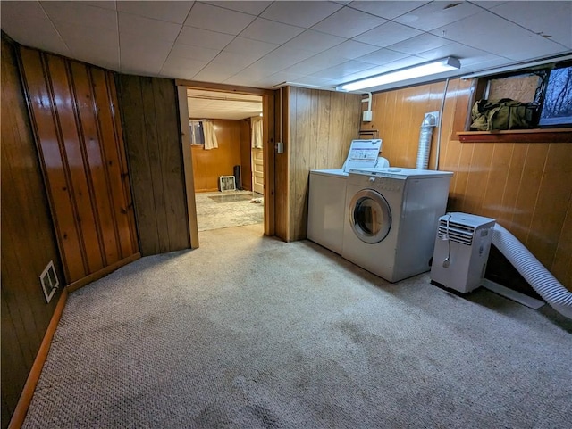 clothes washing area with washing machine and dryer, light colored carpet, and wood walls