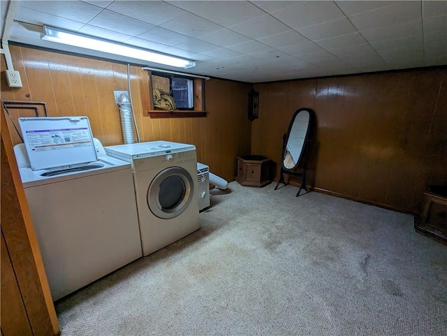 clothes washing area with wooden walls, washer and clothes dryer, and light colored carpet