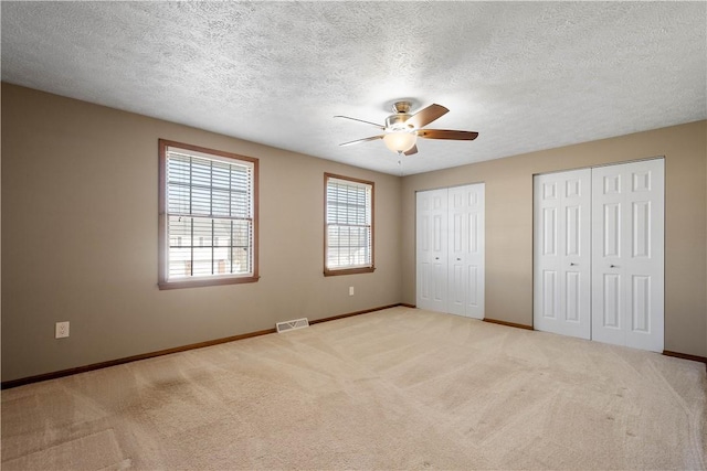 unfurnished bedroom featuring two closets, a textured ceiling, light colored carpet, and ceiling fan