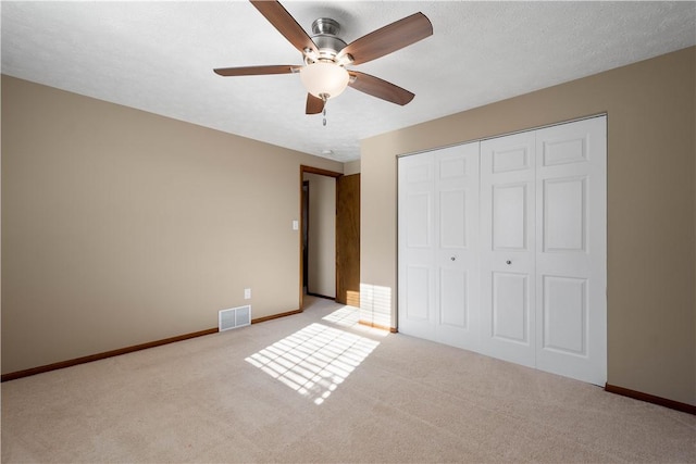 unfurnished bedroom featuring ceiling fan, light colored carpet, a textured ceiling, and a closet