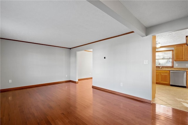 empty room featuring light hardwood / wood-style flooring, beamed ceiling, a textured ceiling, and sink