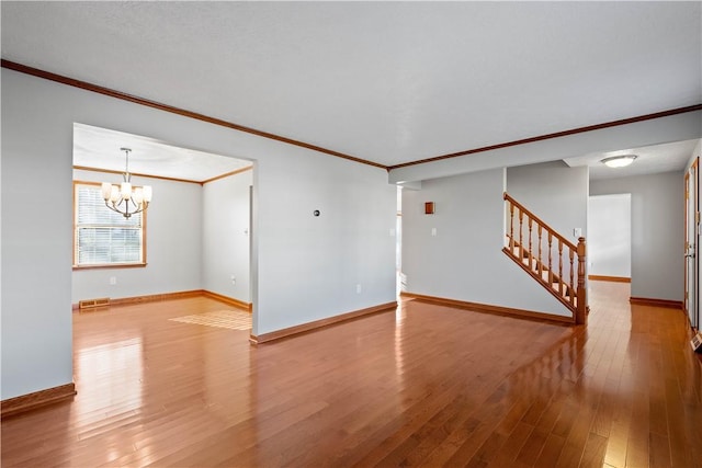 unfurnished living room with hardwood / wood-style flooring, ornamental molding, and an inviting chandelier