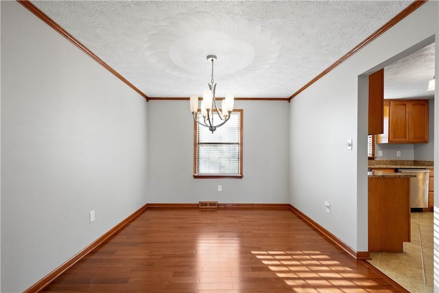 unfurnished dining area featuring hardwood / wood-style floors, ornamental molding, a textured ceiling, and an inviting chandelier