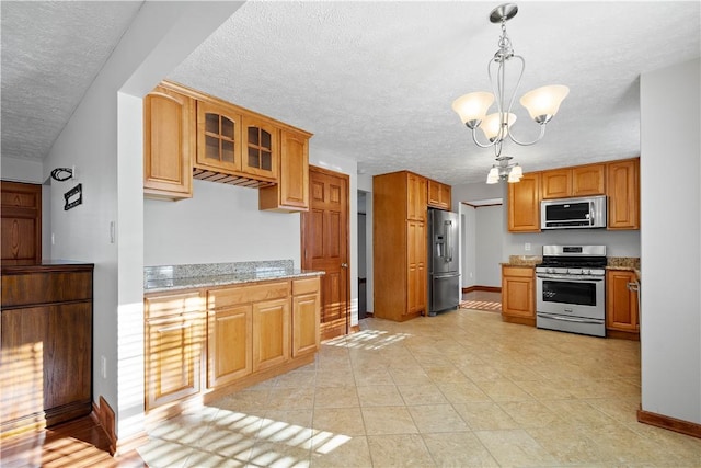 kitchen with hanging light fixtures, a textured ceiling, appliances with stainless steel finishes, light stone counters, and a chandelier