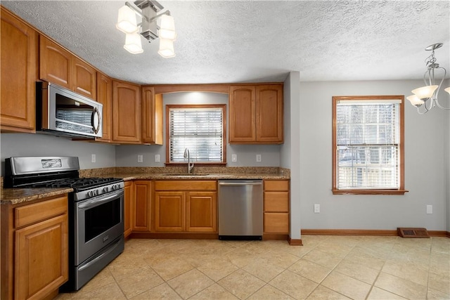 kitchen featuring sink, stainless steel appliances, an inviting chandelier, a textured ceiling, and decorative light fixtures