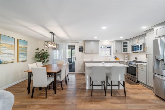 kitchen with light hardwood / wood-style floors, gray cabinetry, pendant lighting, and appliances with stainless steel finishes