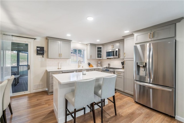 kitchen with a kitchen bar, appliances with stainless steel finishes, tasteful backsplash, and light hardwood / wood-style floors