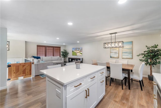 kitchen with white cabinets, decorative light fixtures, a center island, and light hardwood / wood-style flooring