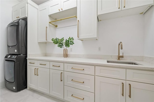 kitchen with stacked washer / dryer, light stone countertops, sink, and white cabinets