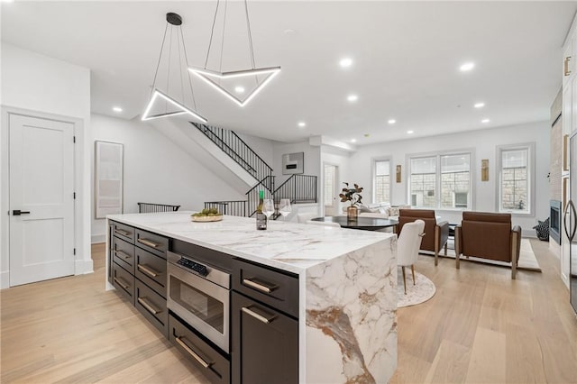 kitchen with pendant lighting, a large island, light hardwood / wood-style flooring, and light stone countertops