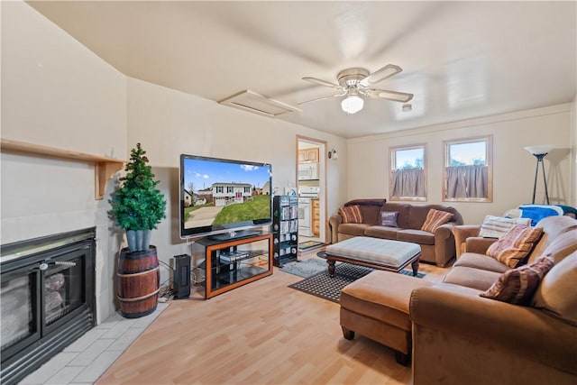 living room featuring ceiling fan, light hardwood / wood-style floors, and a tiled fireplace