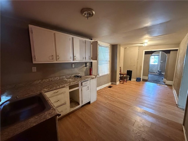 kitchen with white cabinetry, light hardwood / wood-style flooring, dark stone countertops, and sink