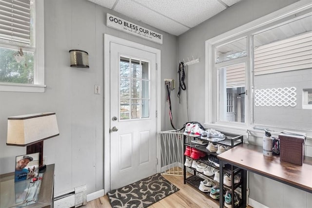 doorway with light hardwood / wood-style flooring, a baseboard radiator, and a drop ceiling