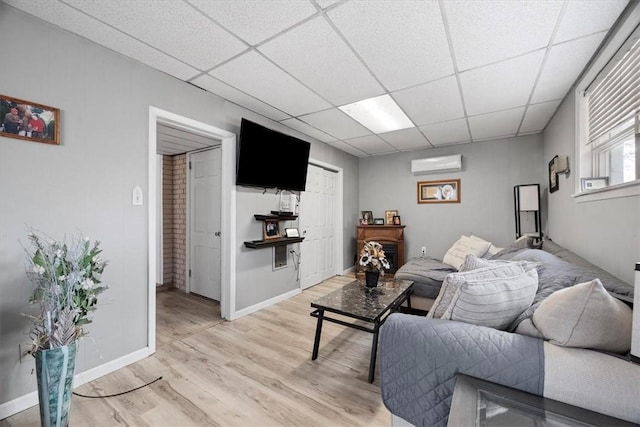 living room featuring a drop ceiling, an AC wall unit, and light hardwood / wood-style flooring