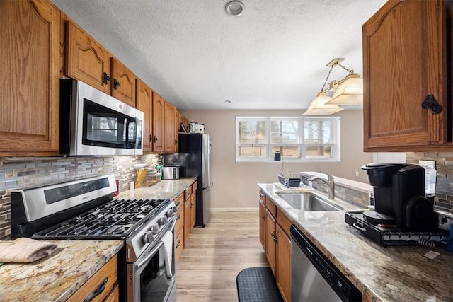 kitchen with backsplash, sink, light stone countertops, light wood-type flooring, and stainless steel appliances