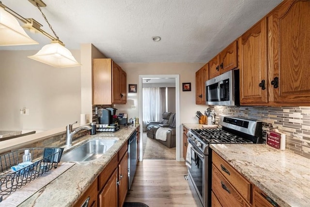 kitchen featuring sink, stainless steel appliances, light hardwood / wood-style flooring, a textured ceiling, and decorative light fixtures