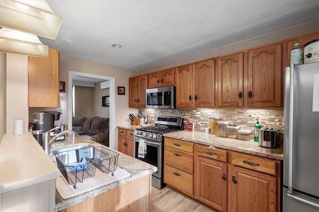 kitchen with sink, light hardwood / wood-style flooring, light stone countertops, tasteful backsplash, and stainless steel appliances