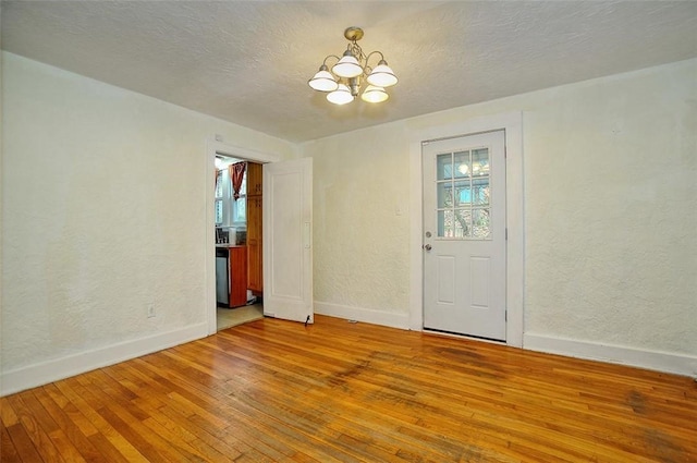 empty room with wood-type flooring, a textured ceiling, and a notable chandelier