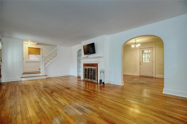 unfurnished living room featuring built in features, light hardwood / wood-style floors, a brick fireplace, and a notable chandelier