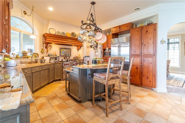 kitchen with built in appliances, a wealth of natural light, a center island, and decorative light fixtures