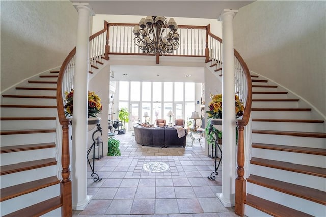 entrance foyer featuring ornate columns, light tile patterned floors, a high ceiling, and an inviting chandelier