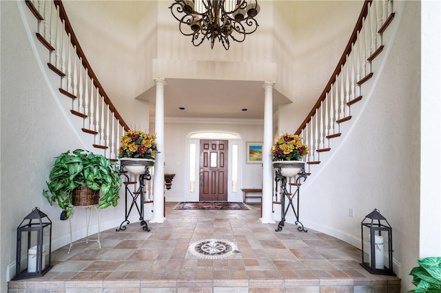 entrance foyer featuring ornate columns, a towering ceiling, a chandelier, and ornamental molding