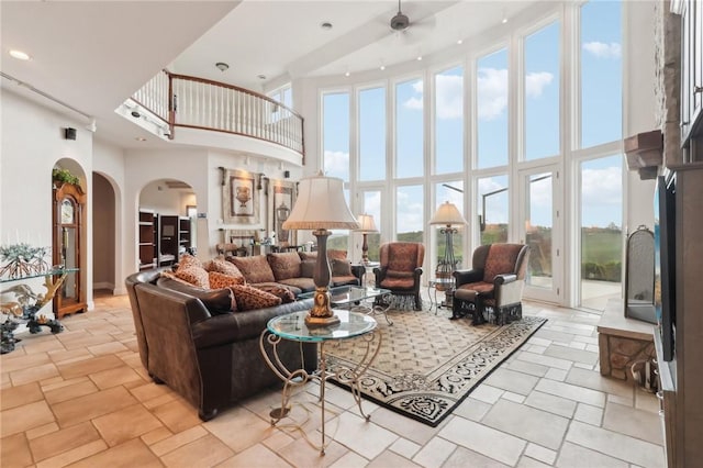 living room featuring arched walkways, a high ceiling, a ceiling fan, and stone finish floor