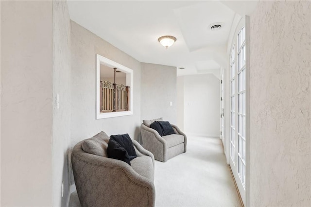 carpeted living area featuring visible vents and a textured wall