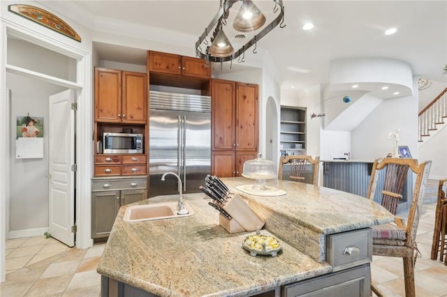 kitchen with light tile patterned flooring, light stone countertops, a sink, stainless steel appliances, and a center island with sink