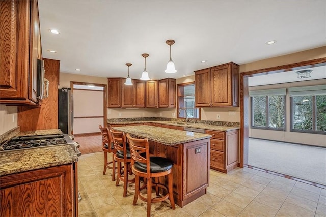 kitchen featuring light stone countertops, sink, decorative light fixtures, a center island, and a breakfast bar area