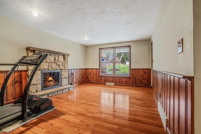 workout area with a fireplace, a textured ceiling, light wood-type flooring, and wood walls