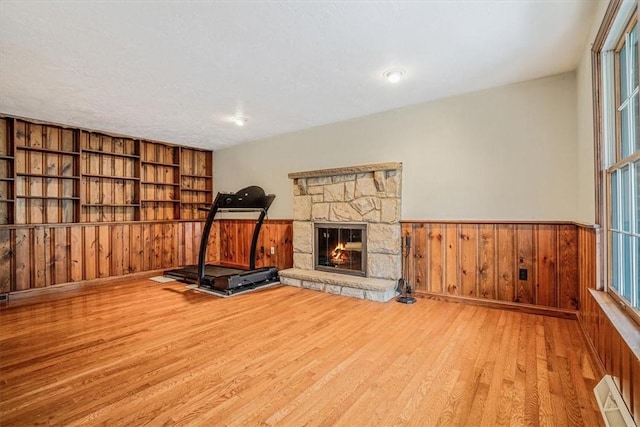 workout area featuring wooden walls, a fireplace, light hardwood / wood-style floors, and a textured ceiling