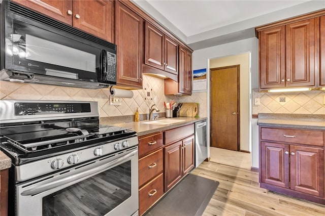 kitchen with sink, decorative backsplash, light wood-type flooring, stone countertops, and stainless steel appliances