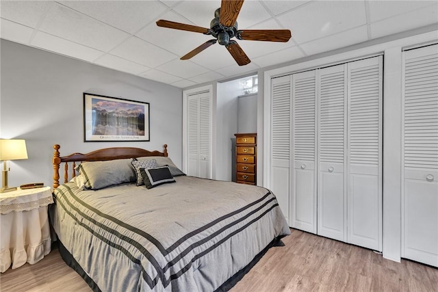 bedroom with light wood-type flooring, a drop ceiling, and multiple closets