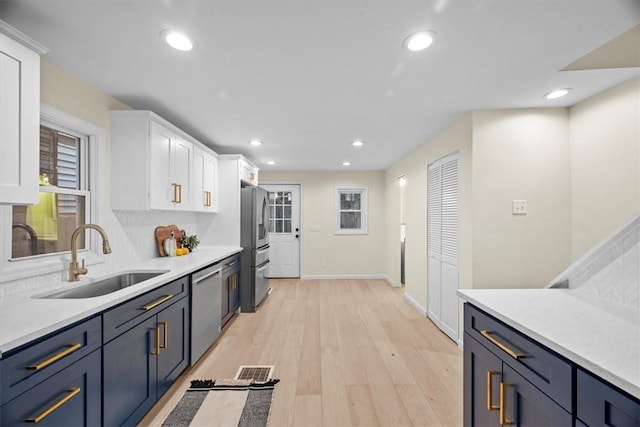 kitchen with stainless steel appliances, blue cabinets, sink, light hardwood / wood-style flooring, and white cabinets