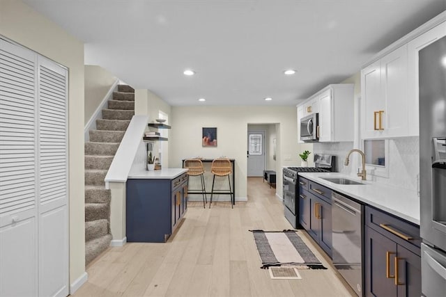 kitchen featuring sink, light wood-type flooring, blue cabinetry, white cabinetry, and stainless steel appliances