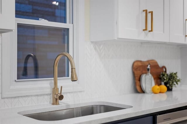 interior details featuring backsplash, dishwasher, sink, and white cabinets