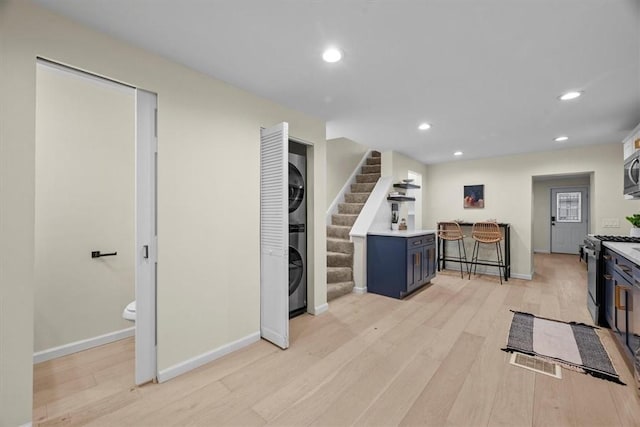 kitchen featuring a kitchen bar, appliances with stainless steel finishes, light wood-type flooring, blue cabinets, and stacked washer / dryer