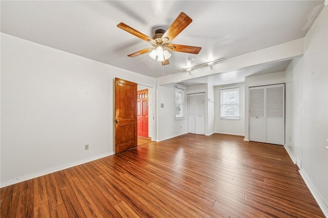 unfurnished bedroom featuring ceiling fan, wood-type flooring, and two closets