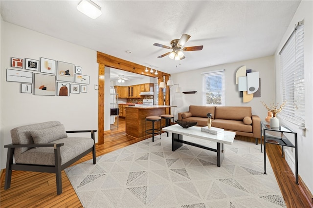 living room with ceiling fan, light wood-type flooring, and a textured ceiling