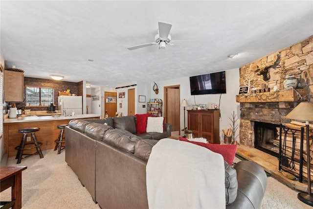 carpeted living room with ceiling fan, a stone fireplace, and sink