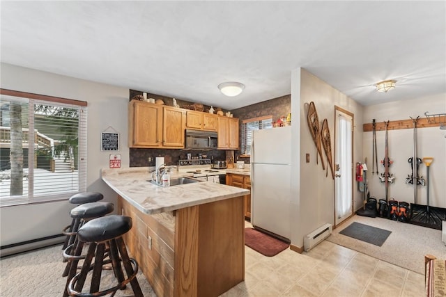 kitchen with sink, baseboard heating, kitchen peninsula, white appliances, and a breakfast bar area