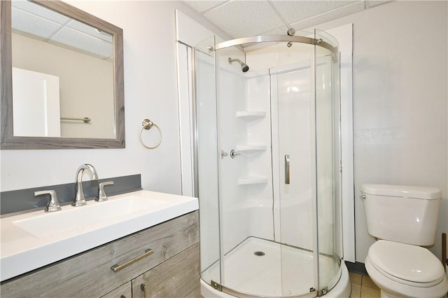 bathroom with tile patterned floors, a drop ceiling, vanity, a shower with door, and toilet