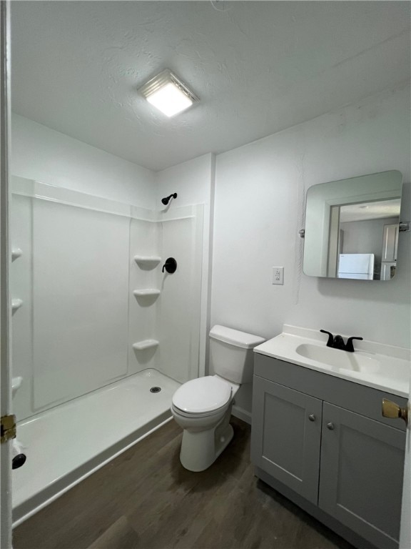 full bathroom with a stall shower, toilet, vanity, and wood finished floors