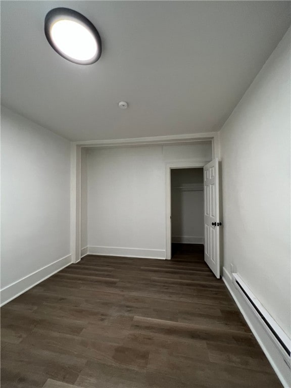 empty room with a baseboard heating unit, baseboards, and dark wood-style flooring