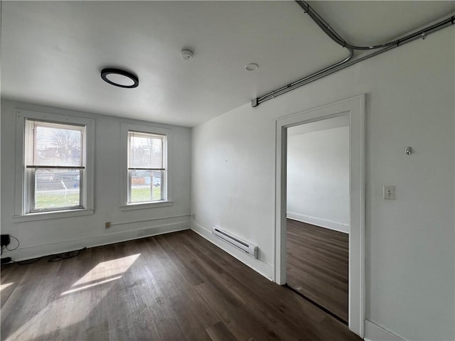 unfurnished room featuring a baseboard heating unit, dark wood finished floors, and baseboards