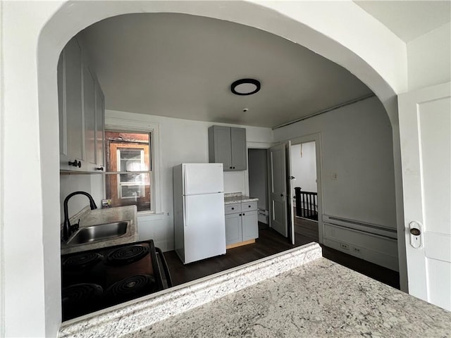 kitchen with dark wood-style flooring, arched walkways, freestanding refrigerator, and a sink