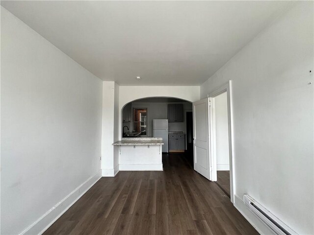 unfurnished living room featuring dark wood-style floors, baseboards, arched walkways, a sink, and baseboard heating