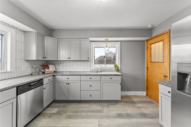 kitchen with appliances with stainless steel finishes, light wood-type flooring, tasteful backsplash, gray cabinetry, and pendant lighting