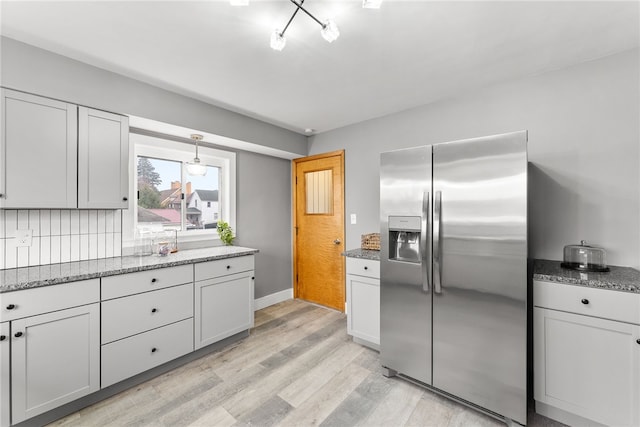 kitchen featuring decorative backsplash, stainless steel fridge with ice dispenser, light wood-type flooring, and stone countertops